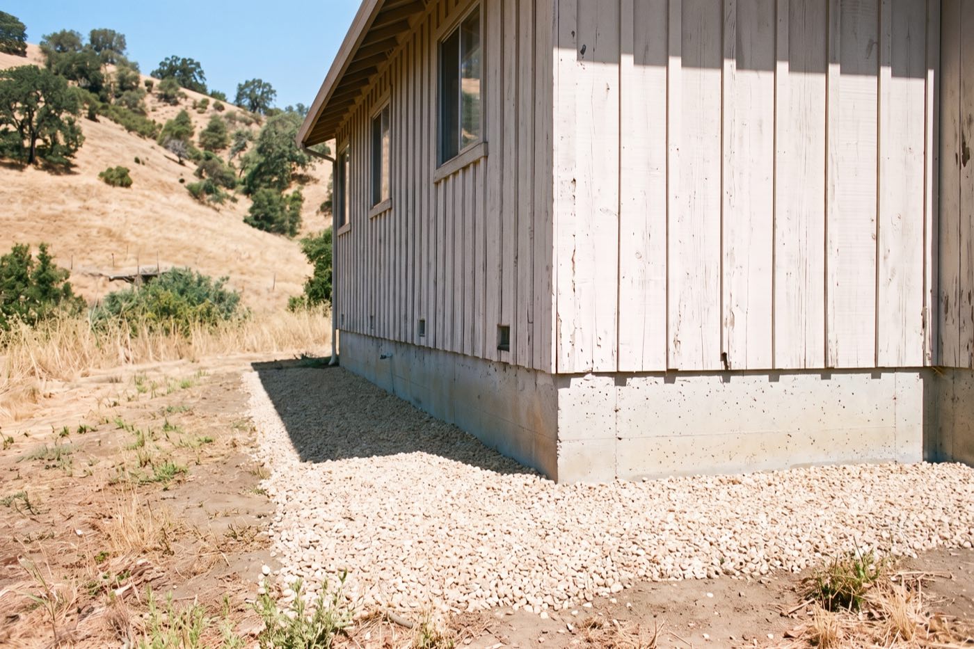 The same wall with the shrub, mulch and woodpile gone and clean gravel along the foundation.